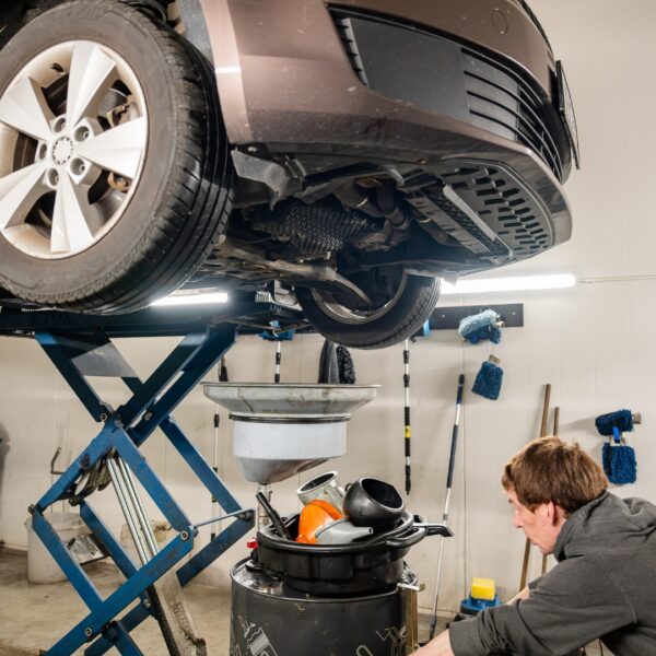 A mechanic working under a car raised on a lift, performing service.