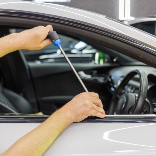 A mechanic unlocking a car window with a special tool.